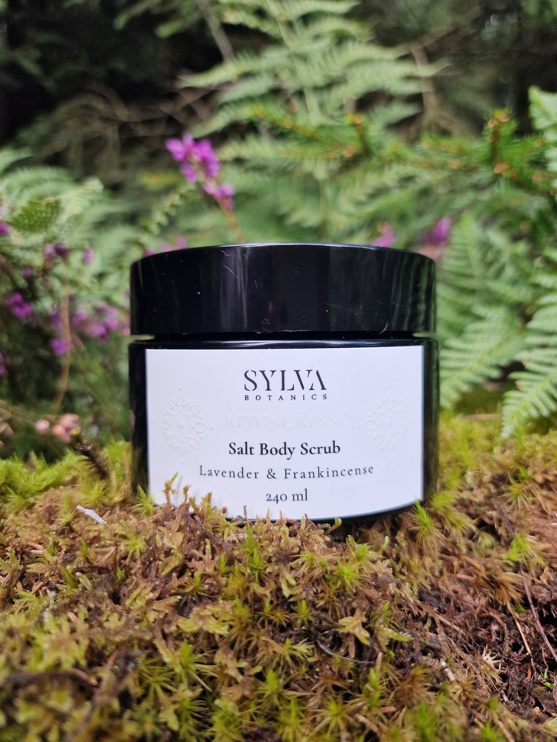 Sylva Botanics Sslt Body Scrub  jar surrounded by forest moss and ferns.